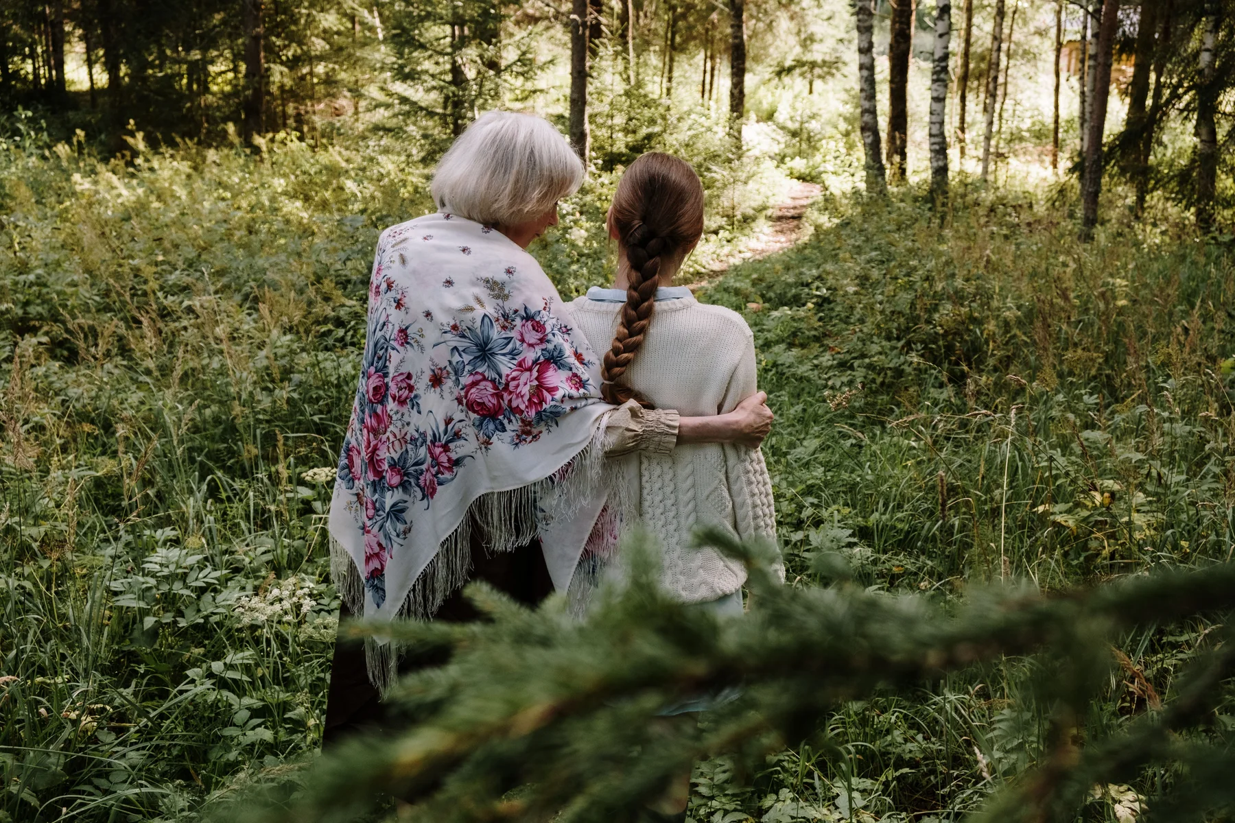 A grandmother embraces her granddaughter on a woodland path